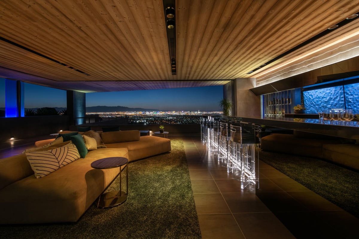Modern high-rise penthouse living room with cityscape views, orange sofa, wooden ceiling, and decorative lighting at dusk